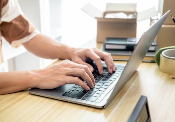 Male entrepreneur is using laptop to checking and taking receive online orders for prepare packing the product into boxes to sending customer while working online shopping delivery at home office.